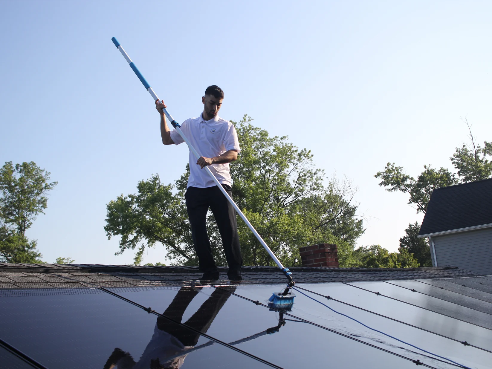 Sunshine Scrubbers technician scrubbing rooftop solar panels with a long soft-bristle brush